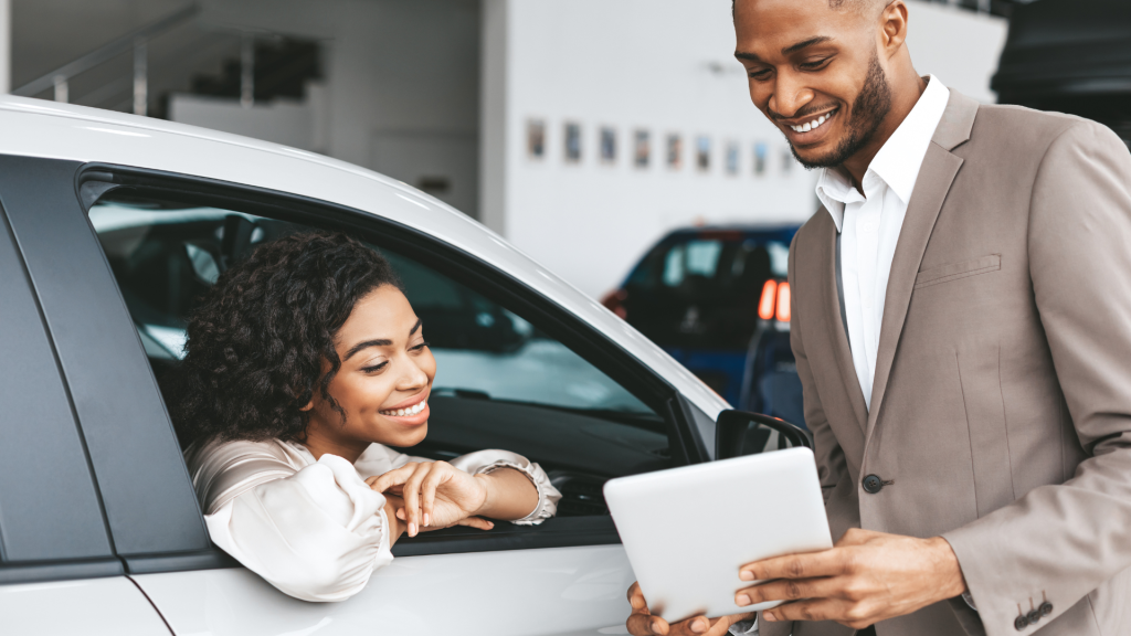 Woman sitting in the passenger seat of a new car in a dealer showroom looking at lease options